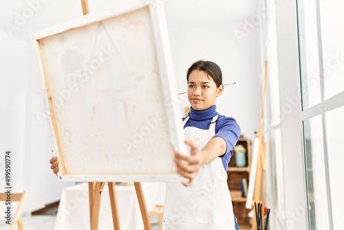 Young latin woman looking canvas draw at art studio