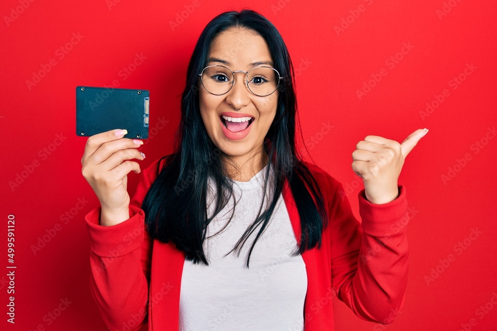 Beautiful hispanic woman with nose piercing holding ssd memory pointing thumb up to the side smiling happy with open mouth Beautiful hispanic woman with nose piercing holding ssd memory pointing thumb up to the side smiling happy with open mouth
