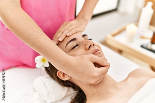 Young hispanic woman smiling confident having facial massage at beauty center.