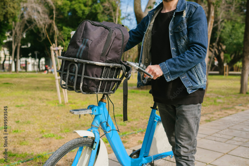 Bike ride, the young man puts his backpack in the basket of the bike and sets off. It holds the handlebar and is ready to ride. green transportation and green park Bike ride, the young man puts his backpack in the basket of the bike and sets off. It holds the handlebar and is ready to ride. green transportation and green park