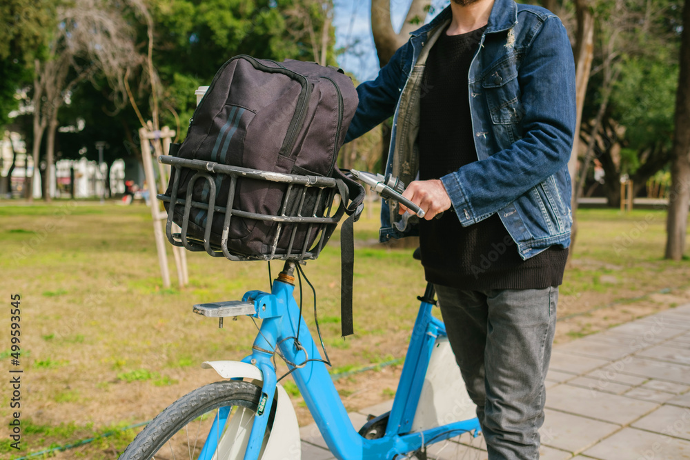 Bike ride, the young man puts his backpack in the basket of the bike and sets off. It holds the handlebar and is ready to ride. green transportation and green park