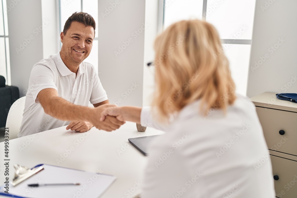 Middle age man and woman doctor and patient shake hands having medical consultation at clinic Middle age man and woman doctor and patient shake hands having medical consultation at clinic