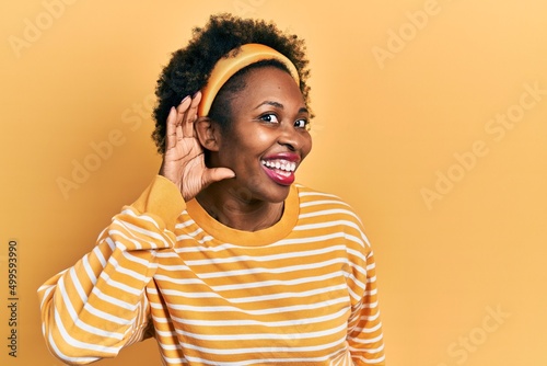 Young african american woman wearing casual sweatshirt smiling with hand over ear listening and hearing to rumor or gossip. deafness concept. © Krakenimages.com
