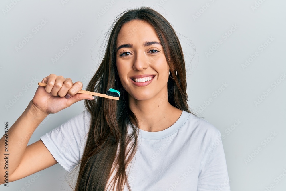 Young hispanic girl holding toothbrush with toothpaste looking positive and happy standing and smiling with a confident smile showing teeth Young hispanic girl holding toothbrush with toothpaste looking positive and happy standing and smiling with a confident smile showing teeth