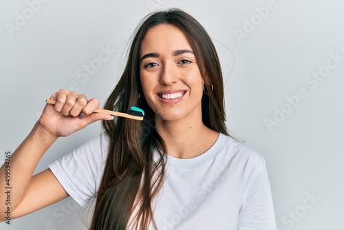 Young hispanic girl holding toothbrush with toothpaste looking positive and happy standing and smiling with a confident smile showing teeth