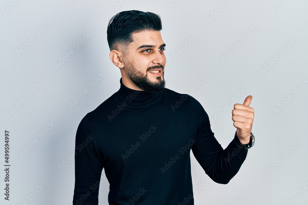 Fototapeta premium Handsome man with beard wearing turtleneck sweater pointing thumb up to the side smiling happy with open mouth
