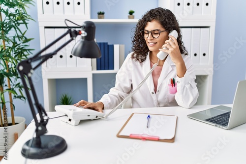 Young latin woman wearing doctor uniform talking on the telephone at clinic