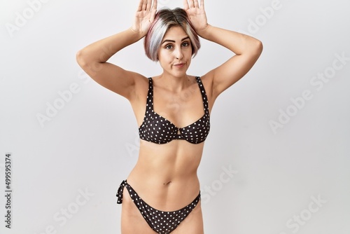 Young beautiful woman wearing swimsuit over isolated background doing bunny ears gesture with hands palms looking cynical and skeptical. easter rabbit concept. photo