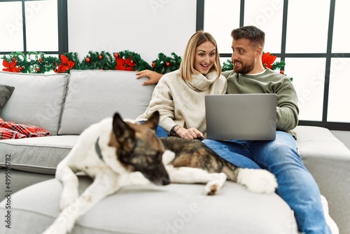 Young caucasian couple smiling happy and using laptop sitting on the sofa with dog at home. © Krakenimages.com