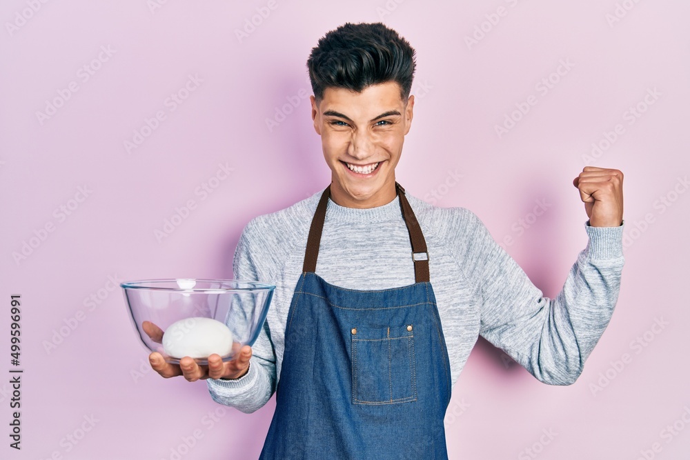 Young hispanic man wearing apron holding bowl of bread dough screaming proud, celebrating victory and success very excited with raised arm Young hispanic man wearing apron holding bowl of bread dough screaming proud, celebrating victory and success very excited with raised arm