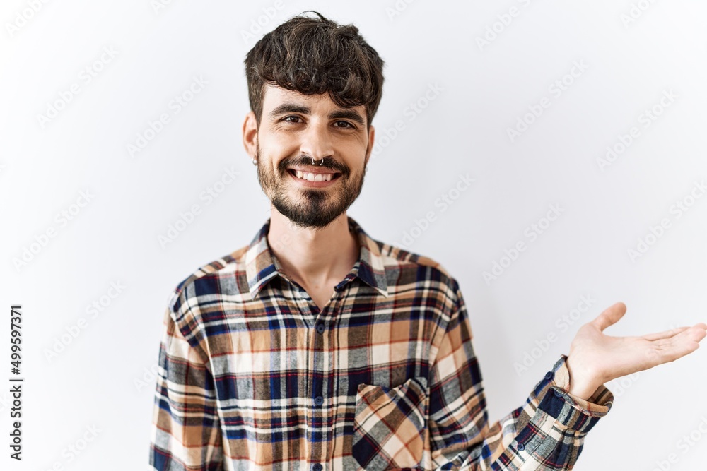 Hispanic man with beard standing over isolated background smiling cheerful presenting and pointing with palm of hand looking at the camera. Hispanic man with beard standing over isolated background smiling cheerful presenting and pointing with palm of hand looking at the camera.