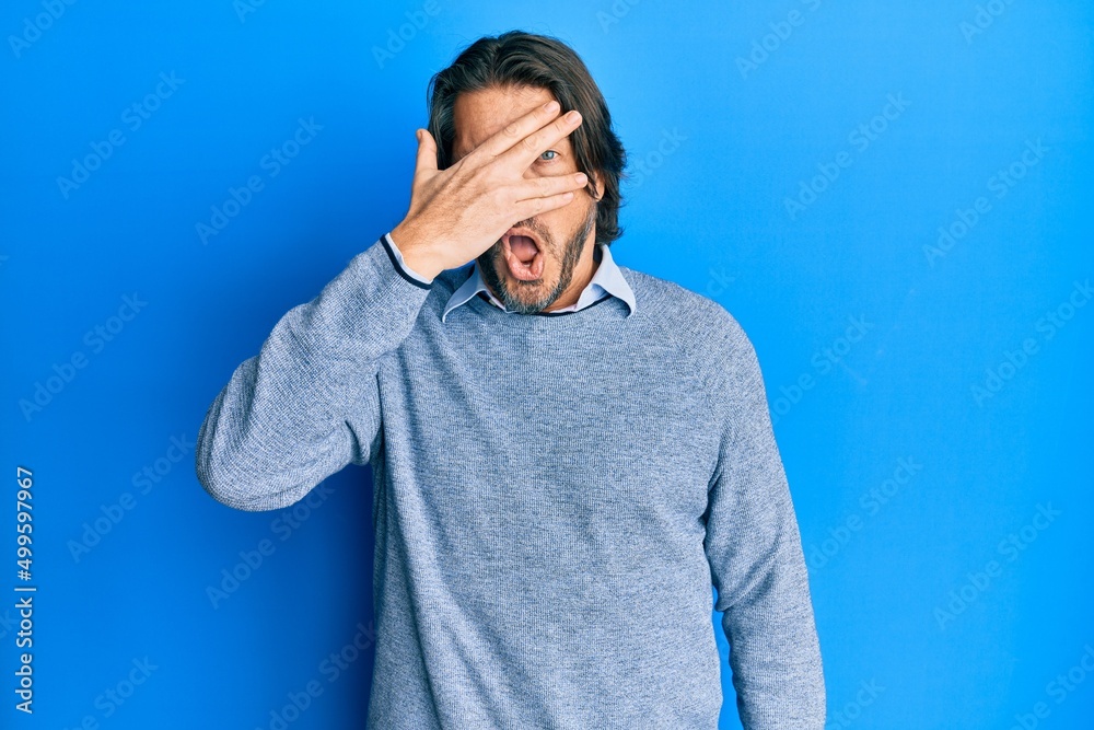 Middle age handsome man wearing casual clothes peeking in shock covering face and eyes with hand, looking through fingers afraid Middle age handsome man wearing casual clothes peeking in shock covering face and eyes with hand, looking through fingers afraid