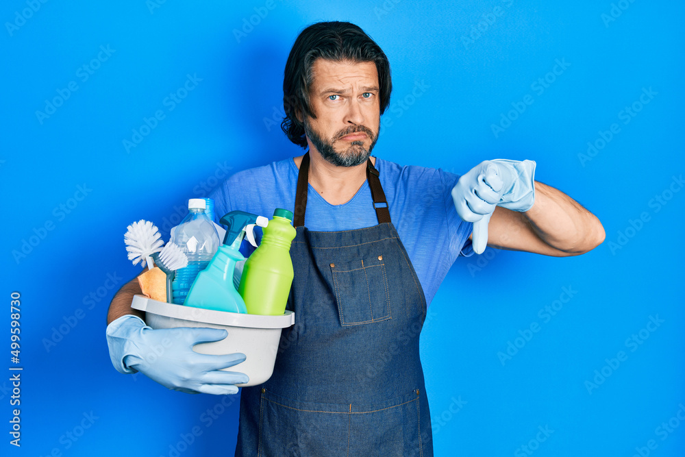 Middle age caucasian man holding cleaning products with angry face, negative sign showing dislike with thumbs down, rejection concept Middle age caucasian man holding cleaning products with angry face, negative sign showing dislike with thumbs down, rejection concept