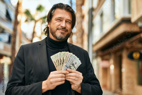 Middle age businessman smiling happy holding dollars at the city.