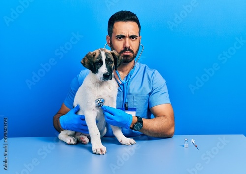 Fototapeta Naklejka Na Ścianę i Meble -  Handsome hispanic veterinary man with beard checking dog health using stethoscope skeptic and nervous, frowning upset because of problem. negative person.