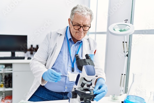 Middle age grey-haired man wearing scientist uniform using microscope at laboratory