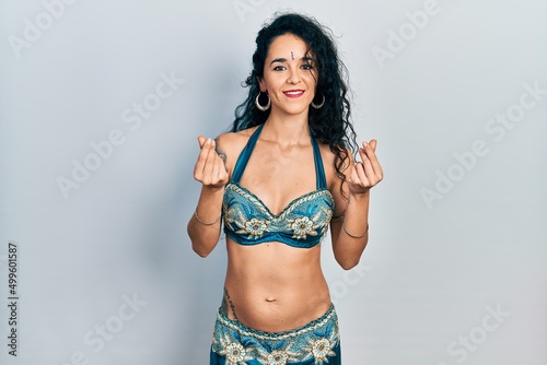 Young woman wearing bindi and traditional belly dance clothes doing money gesture with hands, asking for salary payment, millionaire business