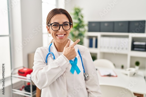 Young brunette doctor woman wearing stethoscope at the clinic cheerful with a smile of face pointing with hand and finger up to the side with happy and natural expression on face