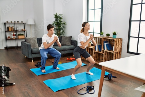 Young caucasian couple concentrate training legs exercise with dog at home.