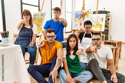 Group of people sitting at art studio pointing with finger to the camera and to you, confident gesture looking serious