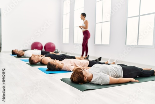 Group of young sporty people relaxed with close eyes lying on the floor on yoga class at sport center.