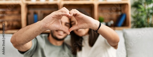 Young latin couple smiling happy doing heart symbol with hands at home.