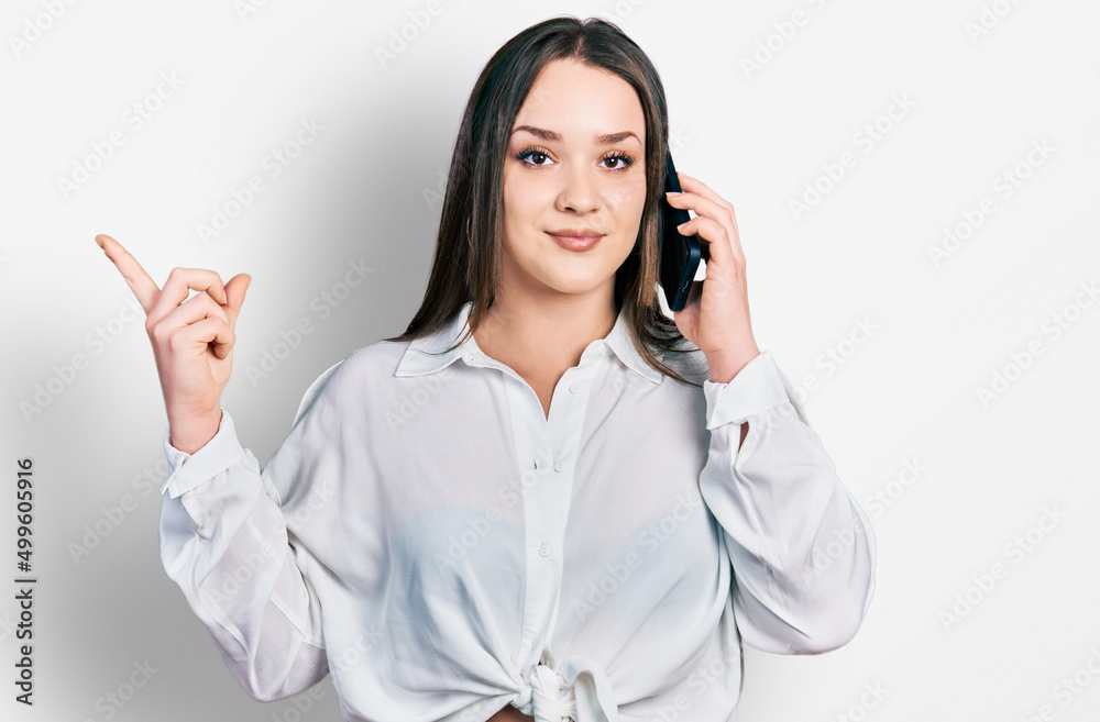 Young hispanic woman having conversation talking on the smartphone smiling happy pointing with hand and finger to the side Young hispanic woman having conversation talking on the smartphone smiling happy pointing with hand and finger to the side