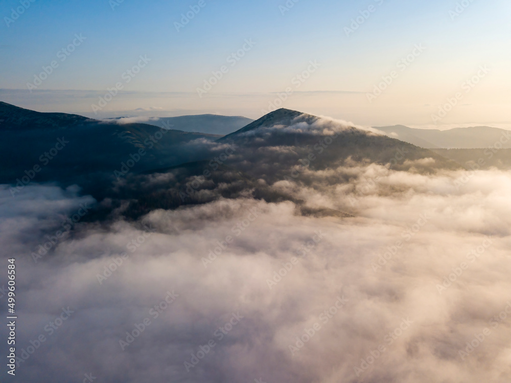 Flight over fog in Ukrainian Carpathians in summer. Mountains on the horizon. Aerial drone view.
