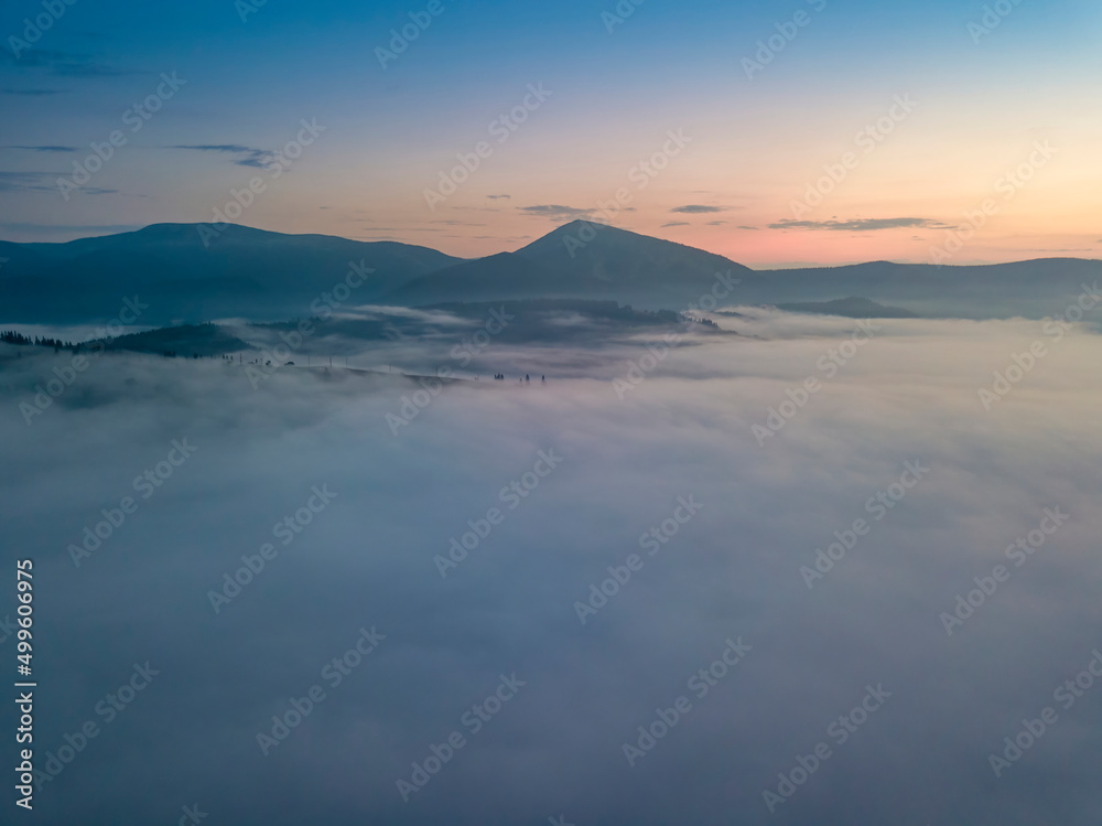 Fototapeta premium The rays of dawn over the fog in the Ukrainian Carpathians. Aerial drone view.