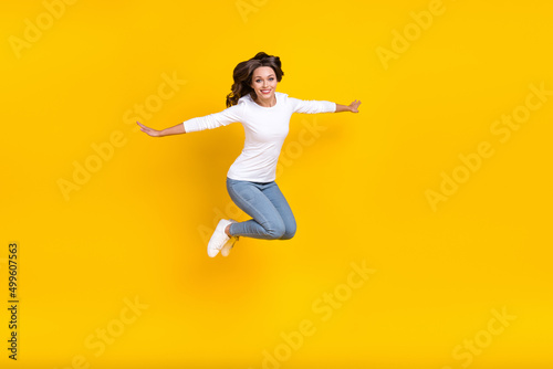 Photo of shiny sweet woman wear white shirt jumping arms sides running isolated yellow color background