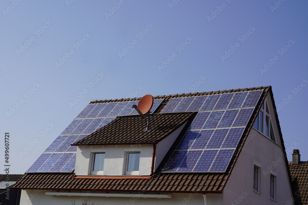Dach von einem kleinen Wohnhaus mit Solar Modulen belegt. Der strahlend blaue Himmel verspricht eine hohe Stromproduktion