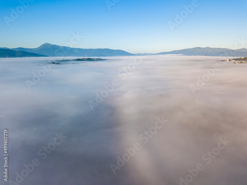 Flight over fog in Ukrainian Carpathians in summer. Mountains on the horizon. A thick layer of fog covers the mountains with a continuous carpet. Aerial drone view.