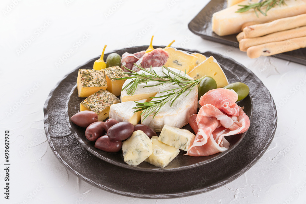 Charcuterie board with assortment of cheeses, salami and prosciutto served with olives on black plate on white table background. Italian traditional antipasti, selective focus