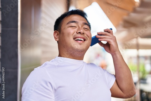 Young chinese man smiling confident listening audio message by the smartphone at street