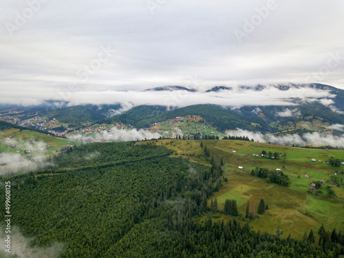 Green slopes of Ukrainian Carpathian mountains in summer. Cloudy morning, low clouds. Aerial drone view.