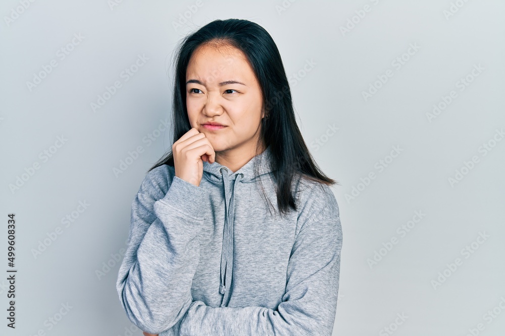 Young chinese girl wearing casual clothes serious face thinking about question with hand on chin, thoughtful about confusing idea Young chinese girl wearing casual clothes serious face thinking about question with hand on chin, thoughtful about confusing idea