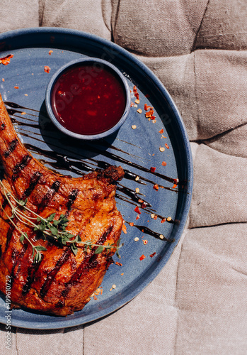 Grilled tomahawk beef steak, with berry sauce, herbs and spices on a blue plate