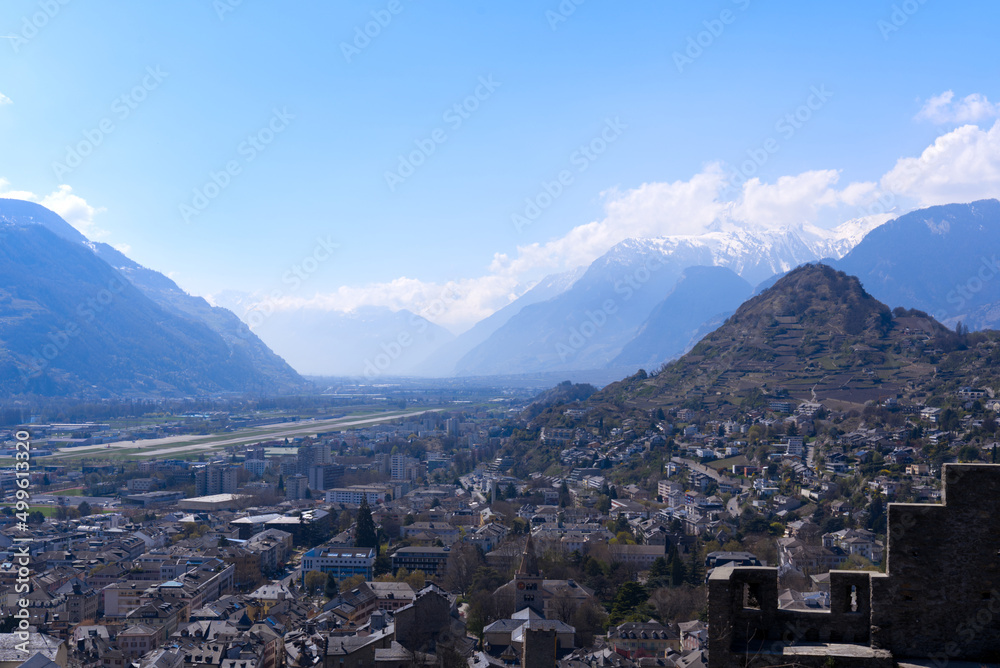 Aerial view from hill of City of Sion over the beautiful landscape of Canton Valais with the Swiss Alps on a blue cloudy spring day. Photo taken April 4th, 2022, Sion, Switzerland.