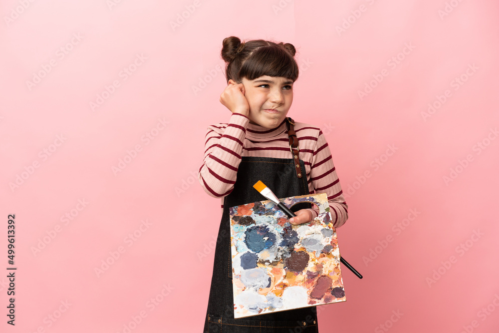 Little artist girl holding a palette isolated on pink background frustrated and covering ears Little artist girl holding a palette isolated on pink background frustrated and covering ears