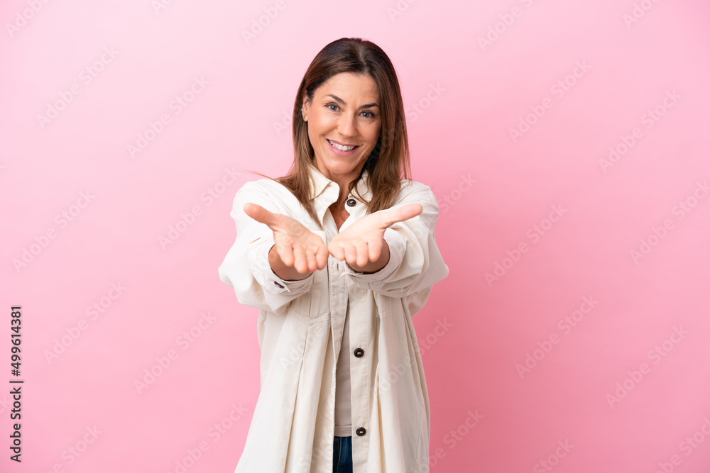 Middle age caucasian woman isolated on pink background holding copyspace imaginary on the palm to insert an ad Middle age caucasian woman isolated on pink background holding copyspace imaginary on the palm to insert an ad