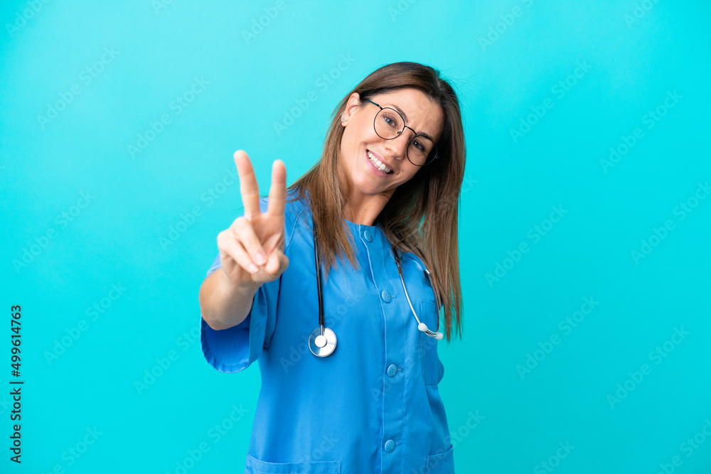 Middle age surgeon woman isolated on blue background smiling and showing victory sign Middle age surgeon woman isolated on blue background smiling and showing victory sign