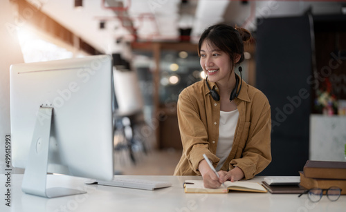 Smiling Asian young female using headset looking at laptop screen listen and learning online courses. Happy business woman with headphones video call for customer service