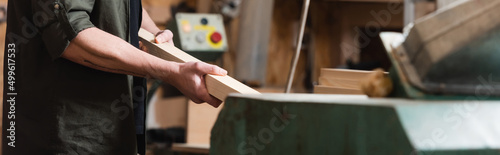 Fotografiet cropped view of furniture designer holding wooden plank in woodwork studio, banner
