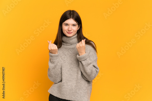 Young Ukrainian girl isolated on yellow background making money gesture but is ruined
