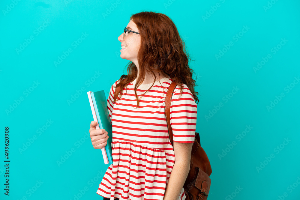 Student teenager redhead girl isolated on blue background laughing in lateral position Student teenager redhead girl isolated on blue background laughing in lateral position