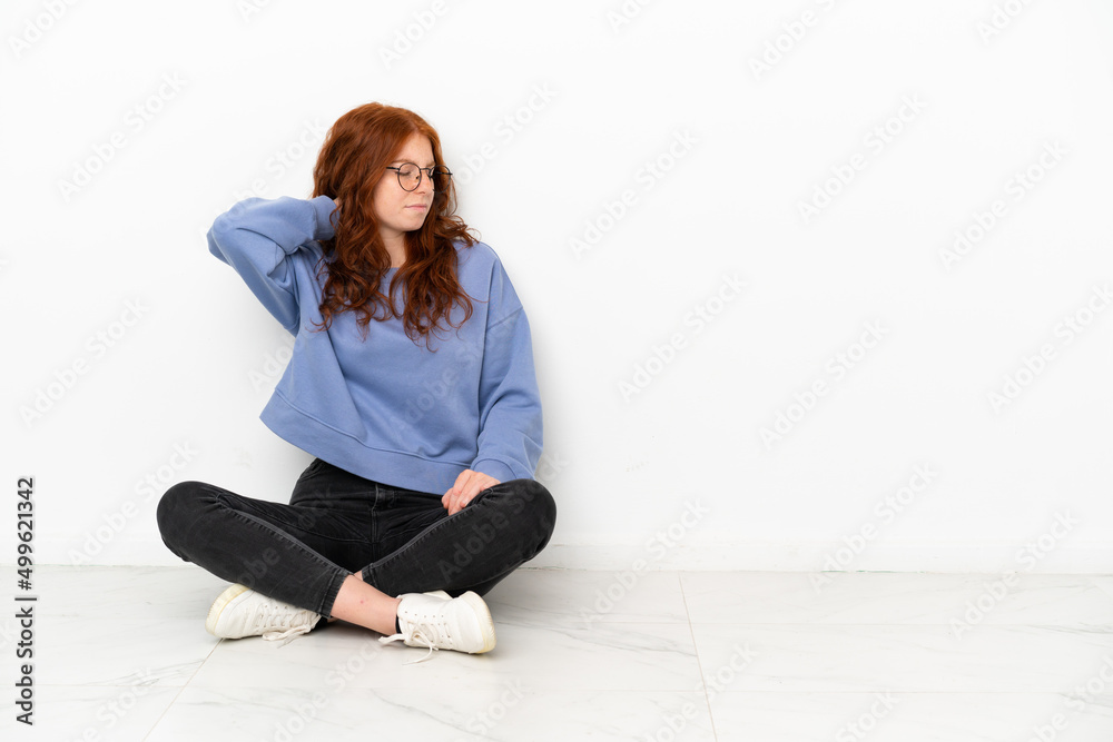 Teenager redhead girl sitting on the floor isolated on white background with neckache Teenager redhead girl sitting on the floor isolated on white background with neckache
