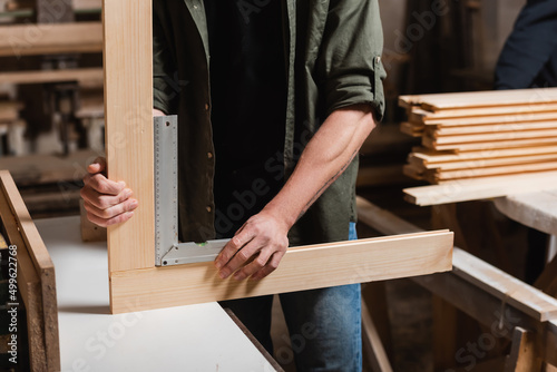 cropped view of furniture designer measuring wooden details with corner ruler.