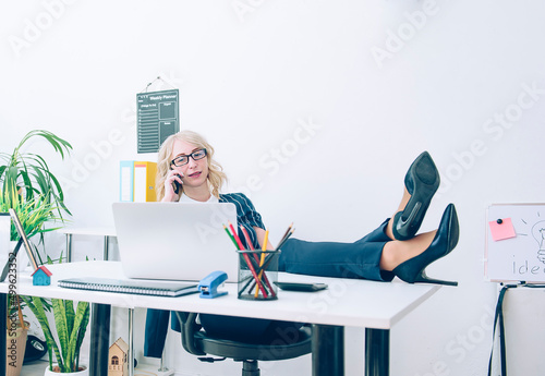 Quadro su tela Businesswoman talking on the phone crossed sexy legs with high heels on a desk in the office