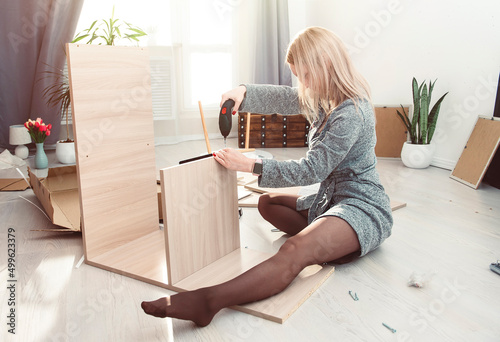 Young woman in a gray robe and sexy legs in tights collects furniture on the floor of the house