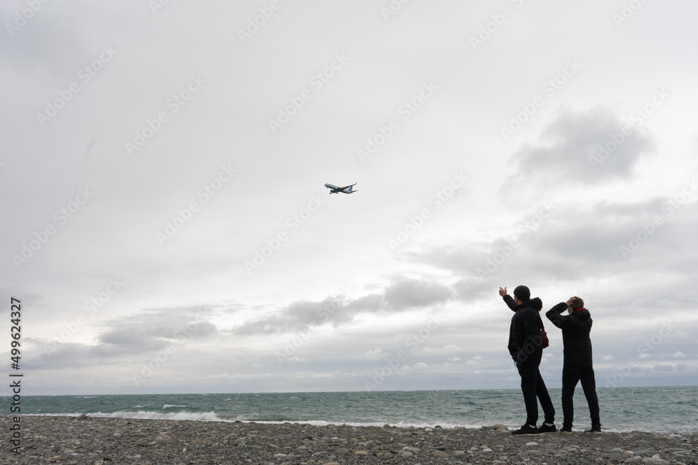 two persons on the beach watch the plane in the sky two persons on the beach watch the plane in the sky